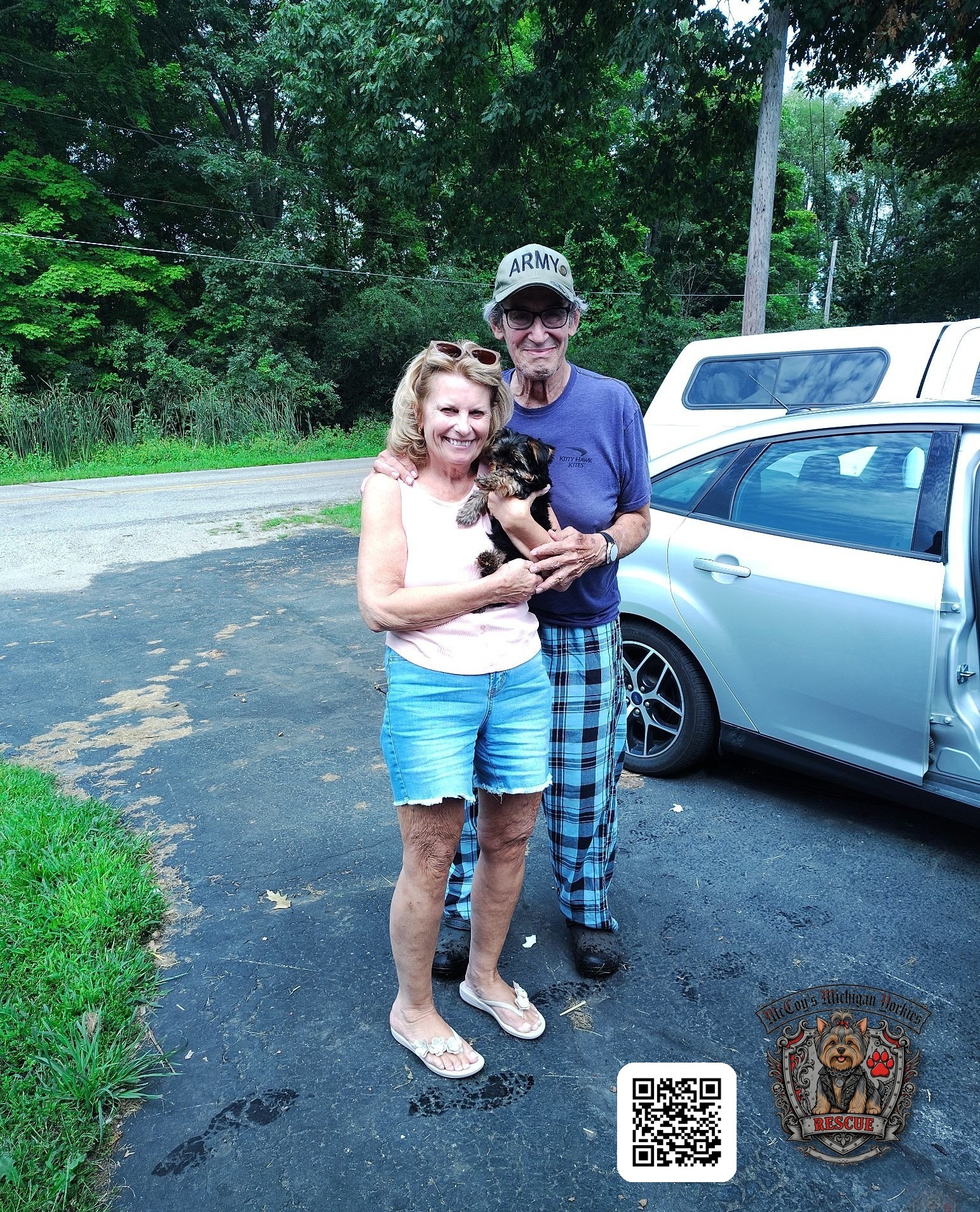 Joe and Sue smiling outdoors while holding their Yorkshire Terrier puppy Riley