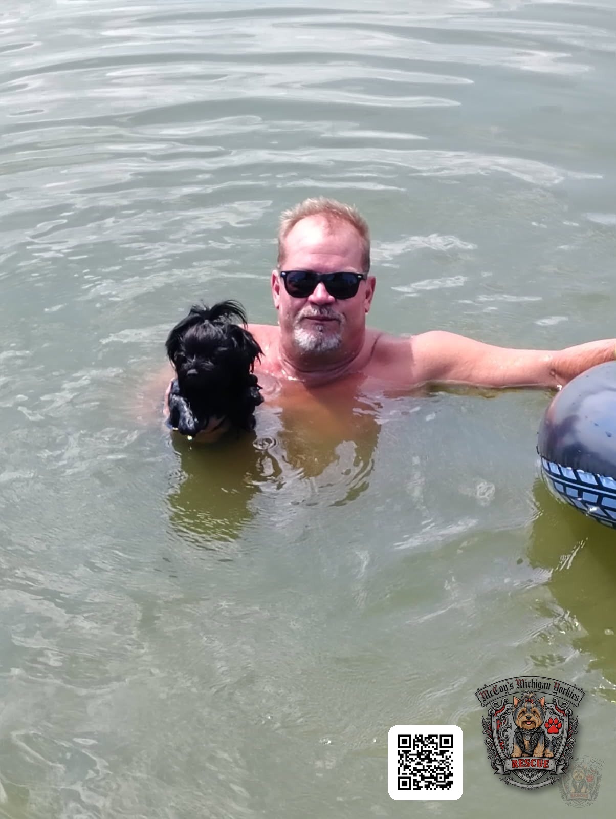 Eric swimming in the lake while holding Waylon, a small black Yorkshire Terrier, safely beside him