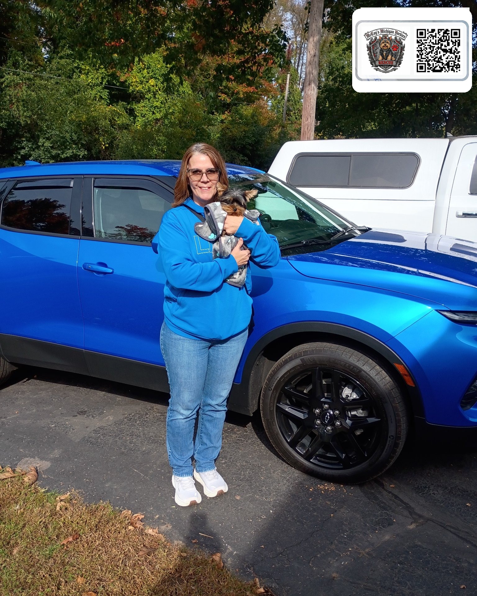 Amy smiling beside her blue SUV while holding Elvis, her tiny Yorkshire Terrier puppy, on gotcha day