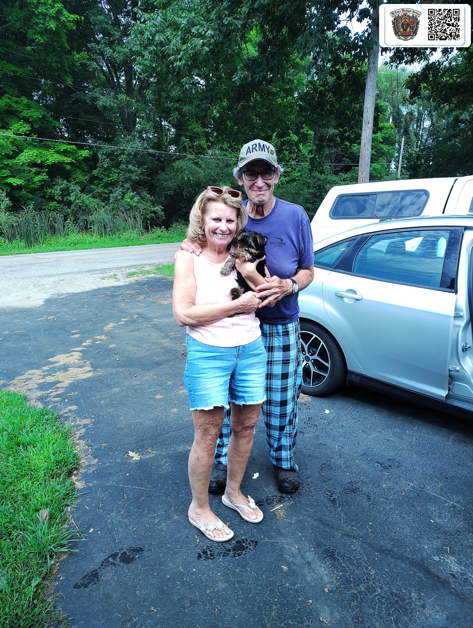 Joe and Sue smiling outdoors while holding their Yorkshire Terrier puppy Riley